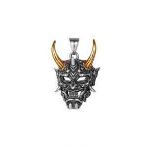 May include: A silver-colored pendant featuring a detailed Oni mask design. The mask has gold-colored horns and intricate facial features, including sharp teeth and piercing eyes. The pendant is suspended from a silver bail.