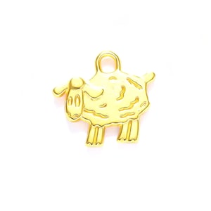 May include: A gold-colored sheep charm with a loop at the top for hanging. The sheep has a detailed face, body, and legs. The charm is likely made of metal and is set against a white background.
