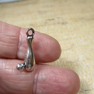 May include: Silver charm of a bowling pin and ball. The charm has a loop at the top for attaching to a necklace or bracelet.