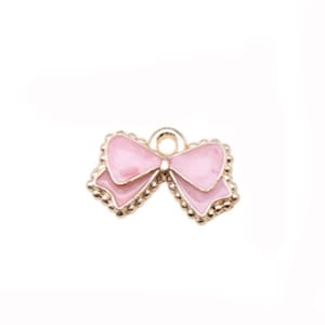 May include: A gold-toned charm with a pink enamel bow. The bow has a loop at the top for attaching to a necklace or bracelet.