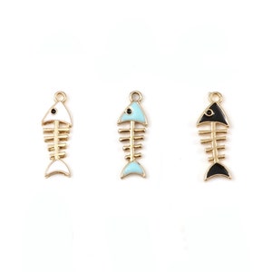 May include: Three fish bone charms in gold-tone metal with enamel accents. One charm has white enamel, another has light blue, and the third has black. Each charm has a small loop at the top for attaching to jewelry.