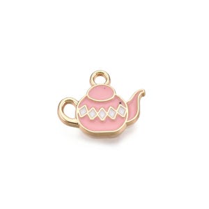 May include: A gold-colored metal charm in the shape of a teapot. The teapot is pink with white diamond-shaped accents and a gold outline. The charm has a loop at the top for attaching to a necklace or bracelet.