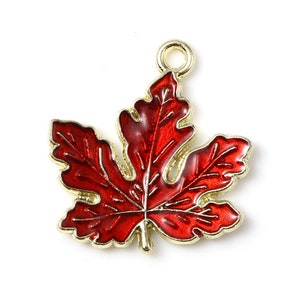 May include: A gold-toned metal maple leaf charm with a red enamel finish. The charm has a loop at the top for attaching to a necklace or bracelet.