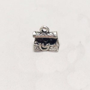 May include: Silver charm in the shape of an ornate treasure chest with a hinged lid. The charm has a loop at the top for attaching to a bracelet or necklace.