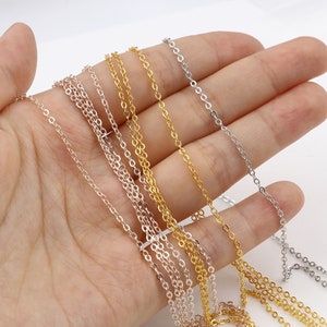 May include: Four different chain styles in silver, gold, and rose gold. The chains are laid out on a hand, showing the different lengths and widths.