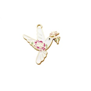 May include: Gold-tone metal charm featuring a white hummingbird with pink and green floral accents. The hummingbird is holding a pink flower in its beak.