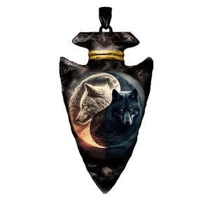 May include: A black arrowhead pendant with a gold-colored band. The pendant features a yin-yang design with two wolves, one white and one black, set against a moonlit background. The pendant is a unique piece of jewelry.