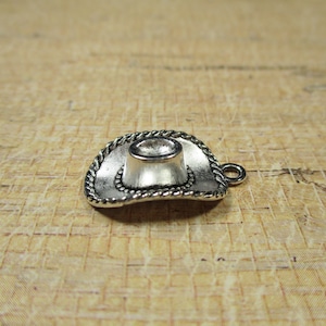 May include: Silver charm in the shape of a cowboy hat. The hat has a rope design around the brim.