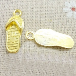 May include: Two gold-colored metal charms shaped like flip-flops. One charm has a textured surface and the other is smooth.