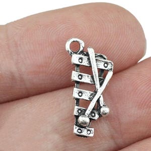 May include: Silver charm in the shape of a xylophone with two mallets. The charm has a loop at the top for attaching to a necklace or bracelet.