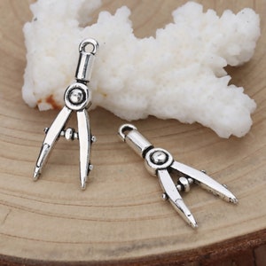 May include: Two silver compass charms with a detailed design. The charms are perfect for jewelry making or adding a unique touch to crafts.