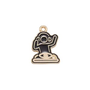 May include: A gold-toned metal charm featuring a black enamel inlay of a stylized figure wearing headphones while operating a turntable. The charm has a small circular loop at the top for attachment, with clean lines and a smooth, polished finish.