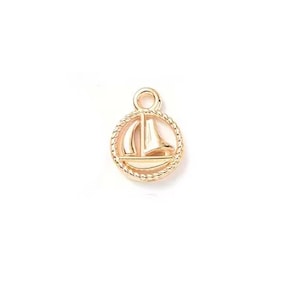 May include: Gold-toned metal charm featuring a sailboat design inside a circle with a rope-like border.