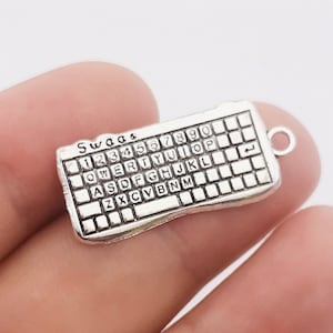 May include: Silver-toned metal charm shaped like a computer keyboard with the letters "Swag" at the top and the keys labeled with numbers and letters. The charm has a loop at the top for attaching to a necklace or bracelet.