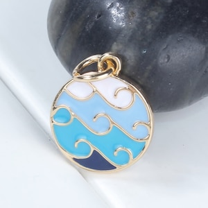 May include: Gold-toned charm with a round blue, white, and light blue enamel design featuring stylized waves.