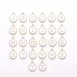 May include: A set of 26 gold-colored metal alphabet charms. Each charm is a white circle with a gold letter in the center. The charms are arranged in alphabetical order.