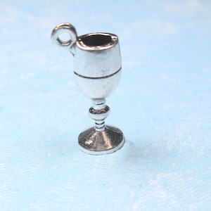 May include: Silver charm in the shape of a goblet or chalice. The charm has a loop at the top for attaching to a bracelet or necklace.