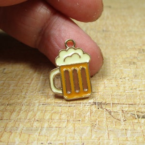 May include: Gold-tone metal charm shaped like a beer mug with a white foam top and orange liquid.