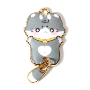 May include: A gold charm with a cartoon cat design. The cat is gray with white accents and a pink nose. The charm has a gold loop at the top and a dangling tail.