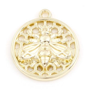 May include: Gold-toned metal charm featuring a bee with detailed wings and body, set against a honeycomb pattern.