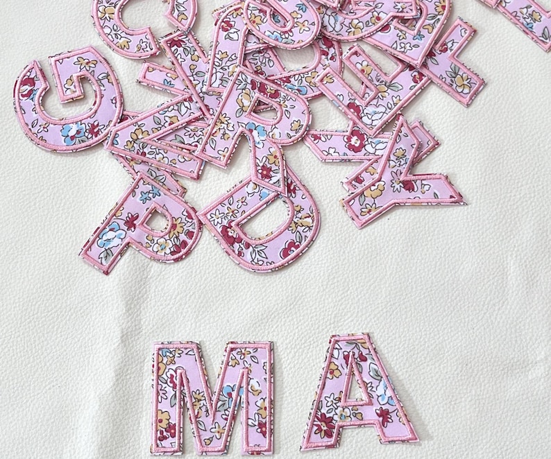 K&ouml;nnte beinhalten: Rosa Stoffbuchstaben mit Blumenmuster. Die Buchstaben ergeben "MA".