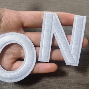 Puede incluir: Letras de fieltro blanco que deletrean la palabra "ON" con un círculo de fieltro blanco.