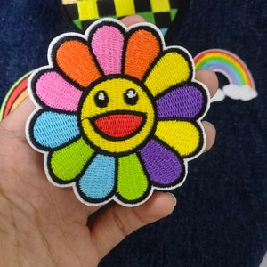May include: A colorful embroidered patch of a smiling flower with a yellow face and rainbow petals.