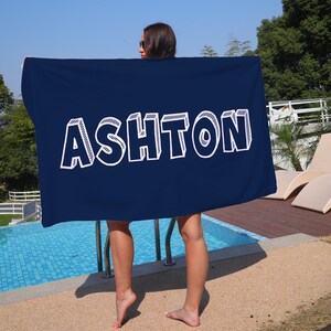 May include: A navy blue beach towel with the name "ASHTON" printed in white outlined letters.