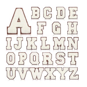 Op de afbeelding: Witte viltletters van het alfabet, van A tot Z, met een bruine omtrek. De letters zijn gerangschikt in drie rijen.