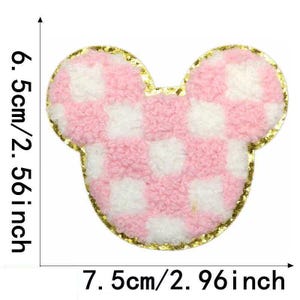 May include: Pink and white checkered fabric applique in the shape of Mickey Mouse ears with a gold outline. The applique is 6.5 inches tall and 7.5 inches wide.