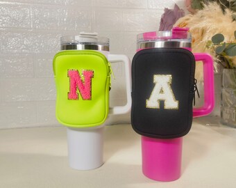 Puede incluir: Dos portavasos aislados con letras personalizadas. El portavasos de la izquierda es verde con una letra N rosa. El portavasos de la derecha es negro con una letra A dorada.
