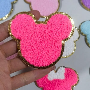 May include: Pink fuzzy Mickey Mouse head shaped patch with a gold glitter outline.