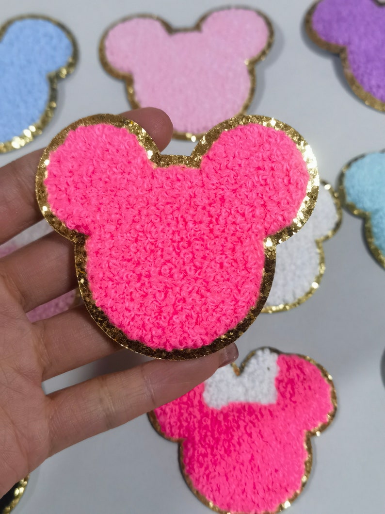 May include: Pink fuzzy Mickey Mouse head shaped patch with a gold glitter outline.