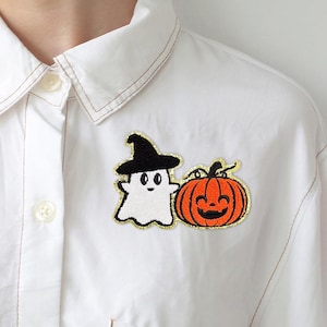 May include: White embroidered ghost wearing a black witch hat and a smiling orange pumpkin with a black stem. The embroidered patches are on a white button-up shirt.