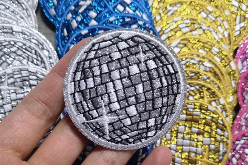 Op de afbeelding: Een ronde, zilveren en zwarte geborduurde strijkpatch van een discobal. De patch is rond en heeft een witte rand.