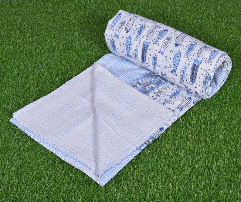 May include: A white and blue kantha quilt with a fish pattern. The quilt is folded in half and rolled up, with the fish pattern visible on the outside.