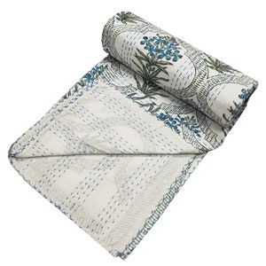 May include: White kantha quilt with a blue and green floral pattern. The quilt is folded and rolled up, showing the stitching detail.