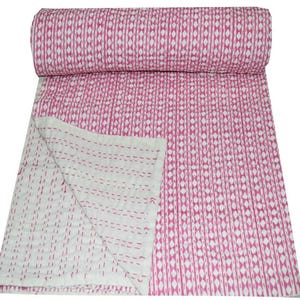 May include: A rolled-up pink and white patterned quilt. The quilt features a repeating vertical design of pink diamonds and white stripes. The underside of the quilt is white with pink stitching. The quilt is made of a soft, lightweight material.