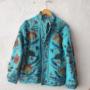 May include: A turquoise jacket with intricate floral embroidery in shades of orange, green, and brown. The jacket features a mandarin collar and a button-up front. The design includes detailed leaf and flower patterns, creating a textured, artistic look.