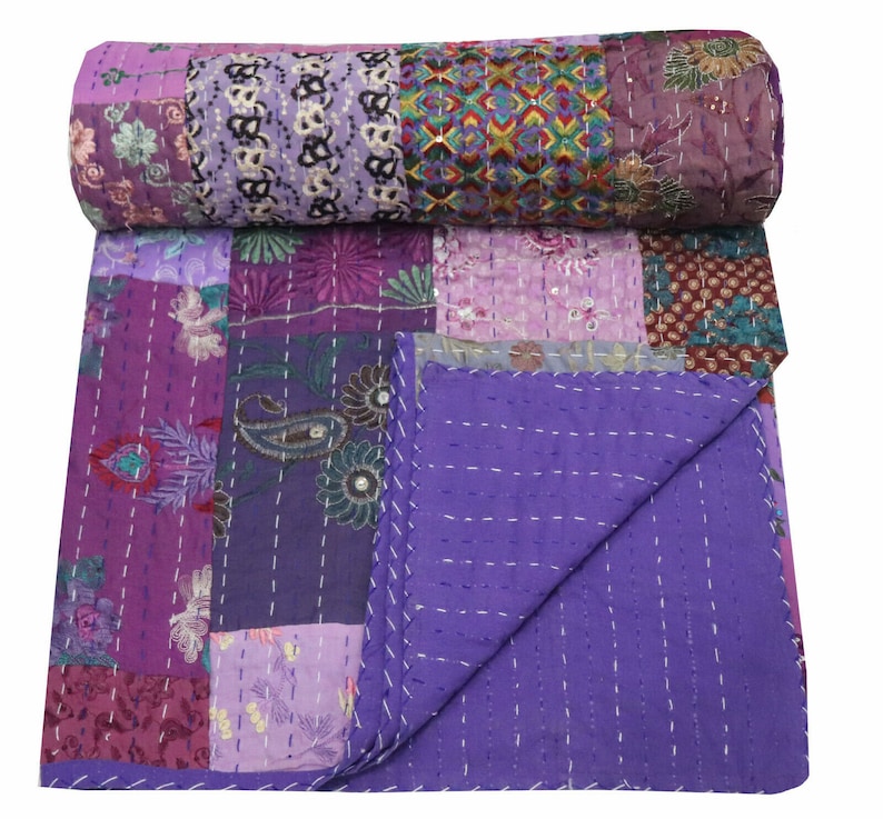 May include: Purple kantha quilt with a patchwork design featuring floral and paisley patterns. The quilt is made of recycled saris and is hand-stitched.