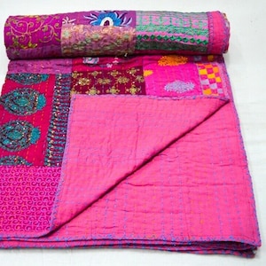 May include: A pink patchwork quilt with various floral and geometric patterns. The quilt is made of different fabrics and is hand-stitched. It is folded in half and laid out on a white surface.