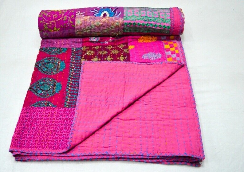 May include: A pink patchwork quilt with various floral and geometric patterns. The quilt is made of different fabrics and is hand-stitched. It is folded in half and laid out on a white surface.