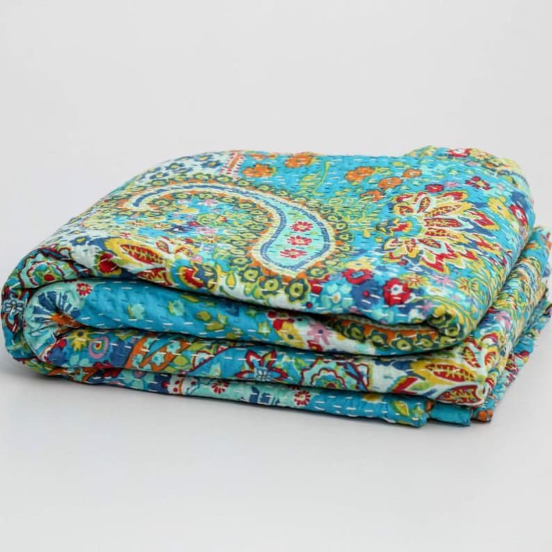 Puede incluir: Una colcha kantha de color azul turquesa doblada con un patr&oacute;n de paisley en tonos de verde, rojo, amarillo y azul.