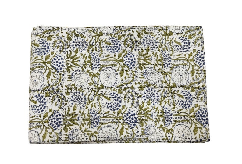 May include: A white cotton quilt with a green and blue floral pattern. The quilt is folded in half and has a stitched edge.