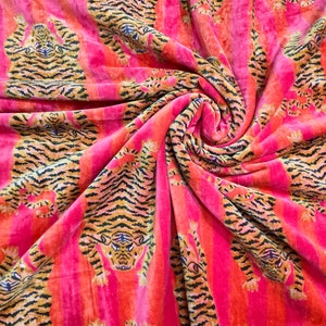 May include: Pink fabric with a repeating pattern of orange and black tigers. The fabric is folded and draped, showing the pattern from different angles.