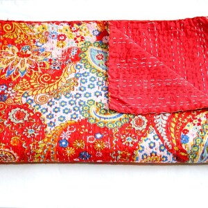 Puede incluir: Una colcha kantha roja y blanca con un patr&oacute;n de paisley. La colcha est&aacute; doblada por la mitad y tiene un respaldo rojo.