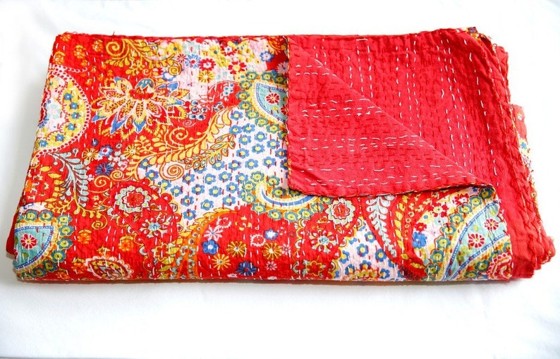 Puede incluir: Una colcha kantha roja y blanca con un patr&oacute;n de paisley. La colcha est&aacute; doblada por la mitad y tiene un respaldo rojo.