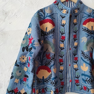 Peut inclure: Veste bleu clair avec broderies florales d&eacute;taill&eacute;es en rouge, jaune et vert. La veste a un col mandarin et une doublure ray&eacute;e. La broderie pr&eacute;sente des fleurs et des feuilles stylis&eacute;es, cr&eacute;ant un design color&eacute;.