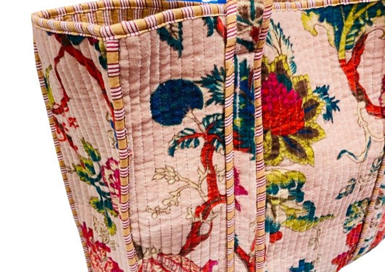 May include: A pink quilted tote bag with a floral print and striped trim. The bag has two handles and a zipper closure.