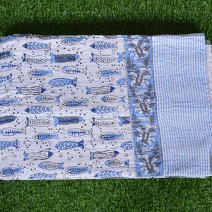 May include: A white and blue cotton quilt with a pattern of blue fish and floral designs. The quilt has a light blue border with white stripes.